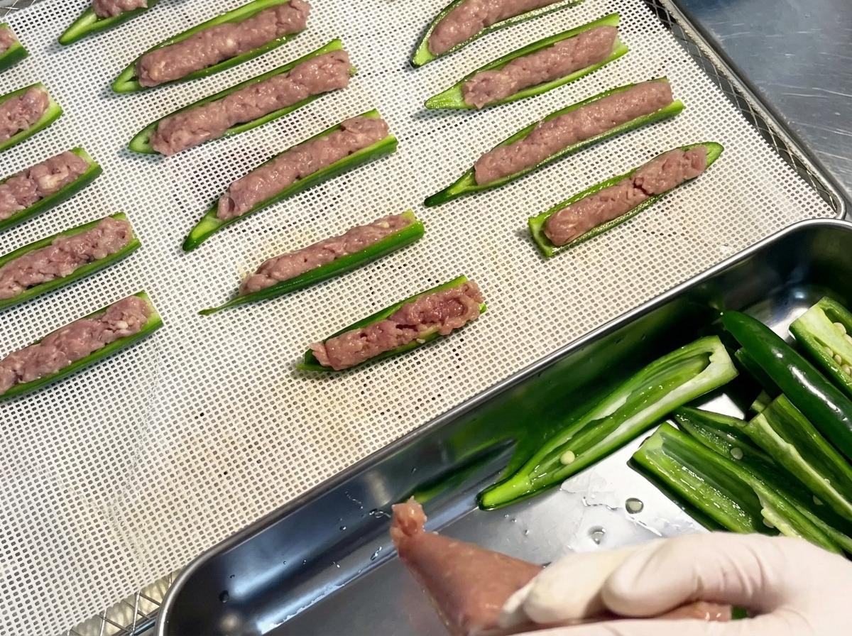 Filled raw okra boats arranged neatly in rows on a white plastic mesh dehydrator tray.