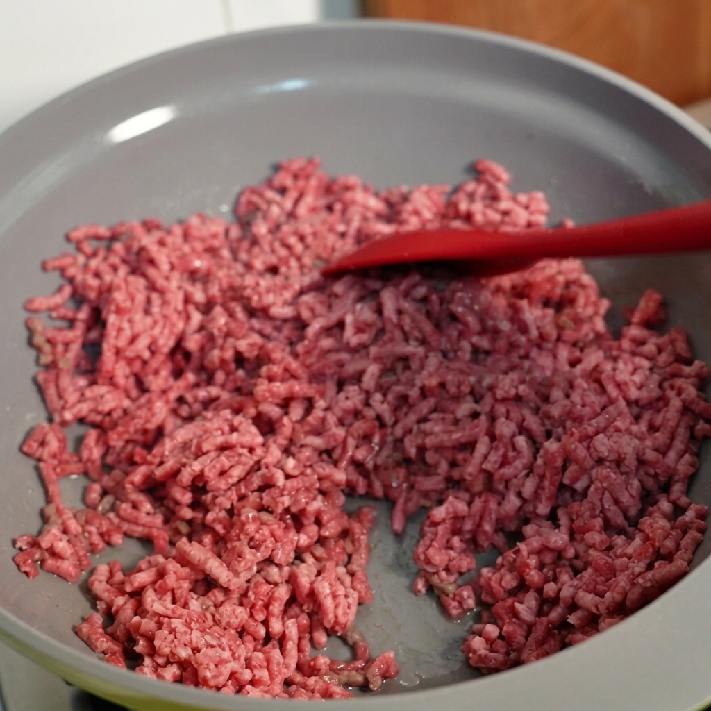 Ground beef being stirred in a skillet, showing browned texture.