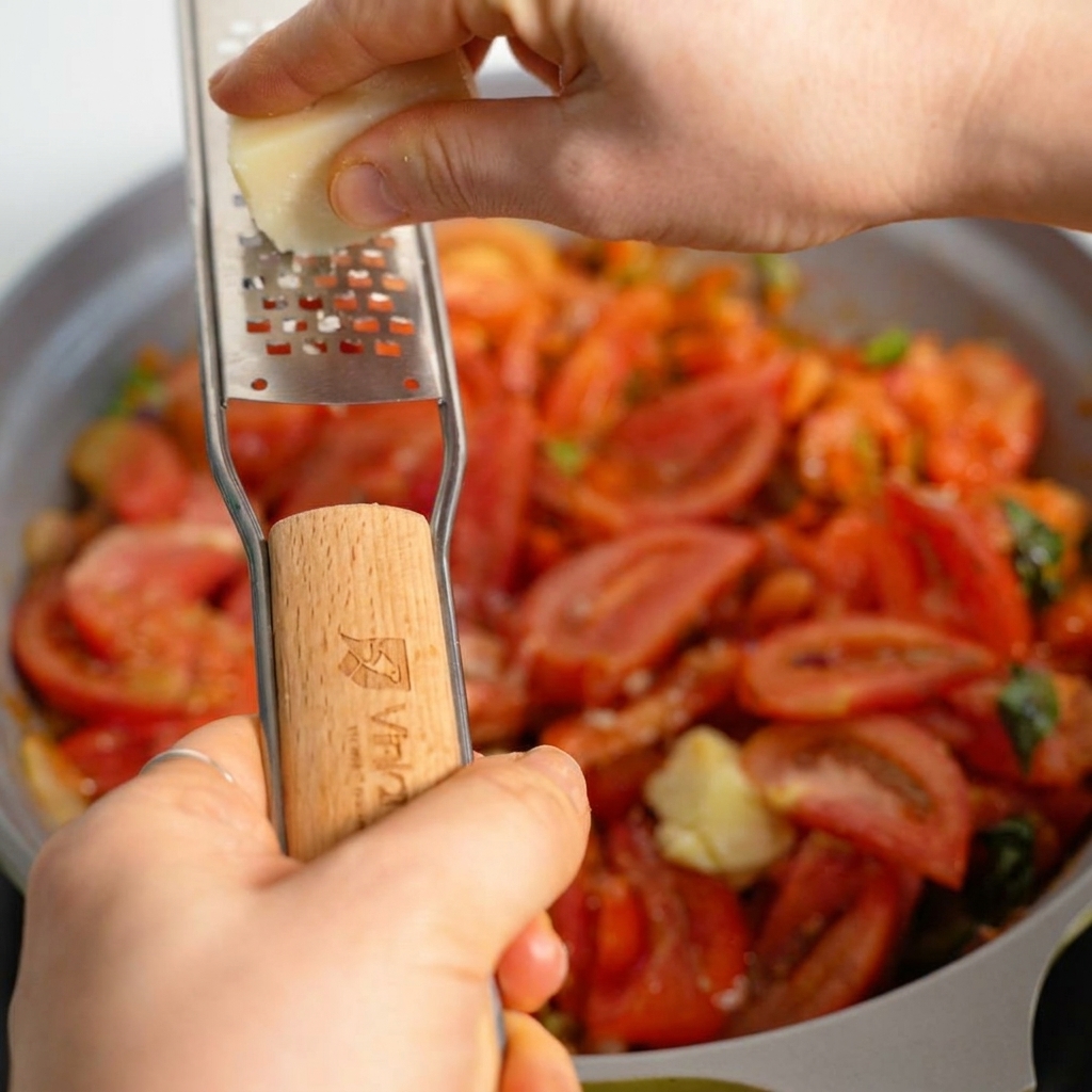 Fresh Parmesan cheese being grated over a bubbling, hearty tomato meat sauce in a skillet.