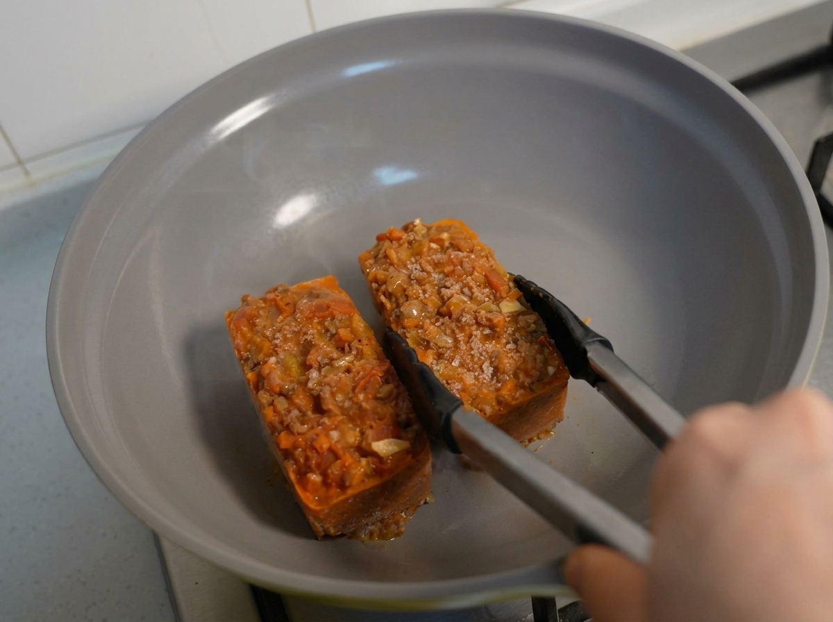 Frozen blocks of meal-prepped pasta and meat sauce being heated in a skillet with tongs.