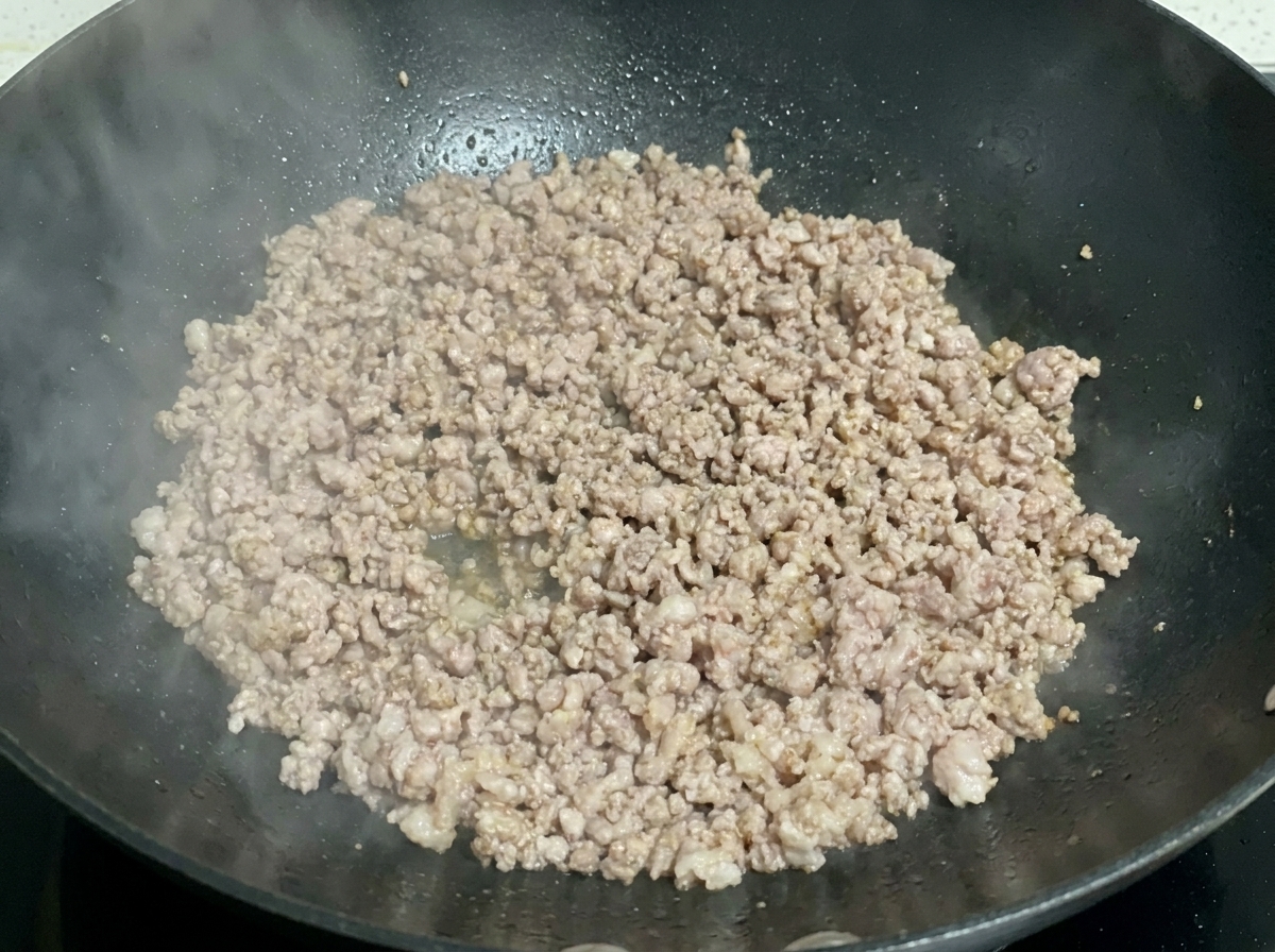 Cooked and slightly browned minced pork crumbles sizzling in a dark wok.
