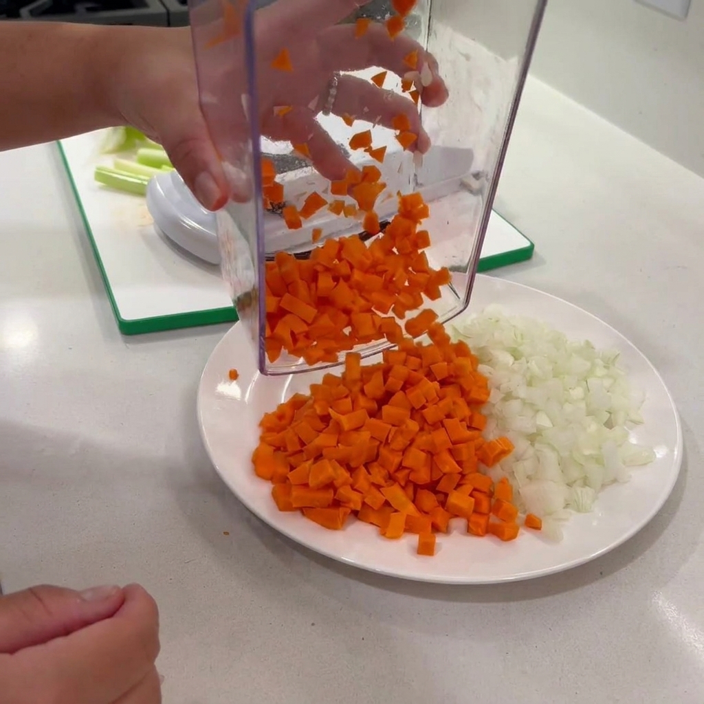 Diced carrots being dispensed from a clear vegetable chopper onto a plate with onions.
