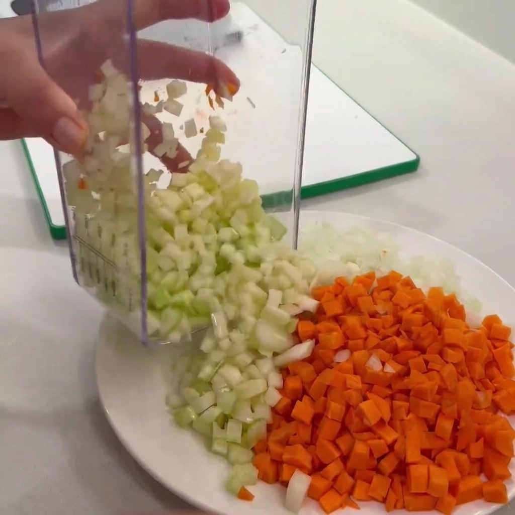 Diced celery being emptied from a clear chopper onto a plate alongside diced carrots and onions.