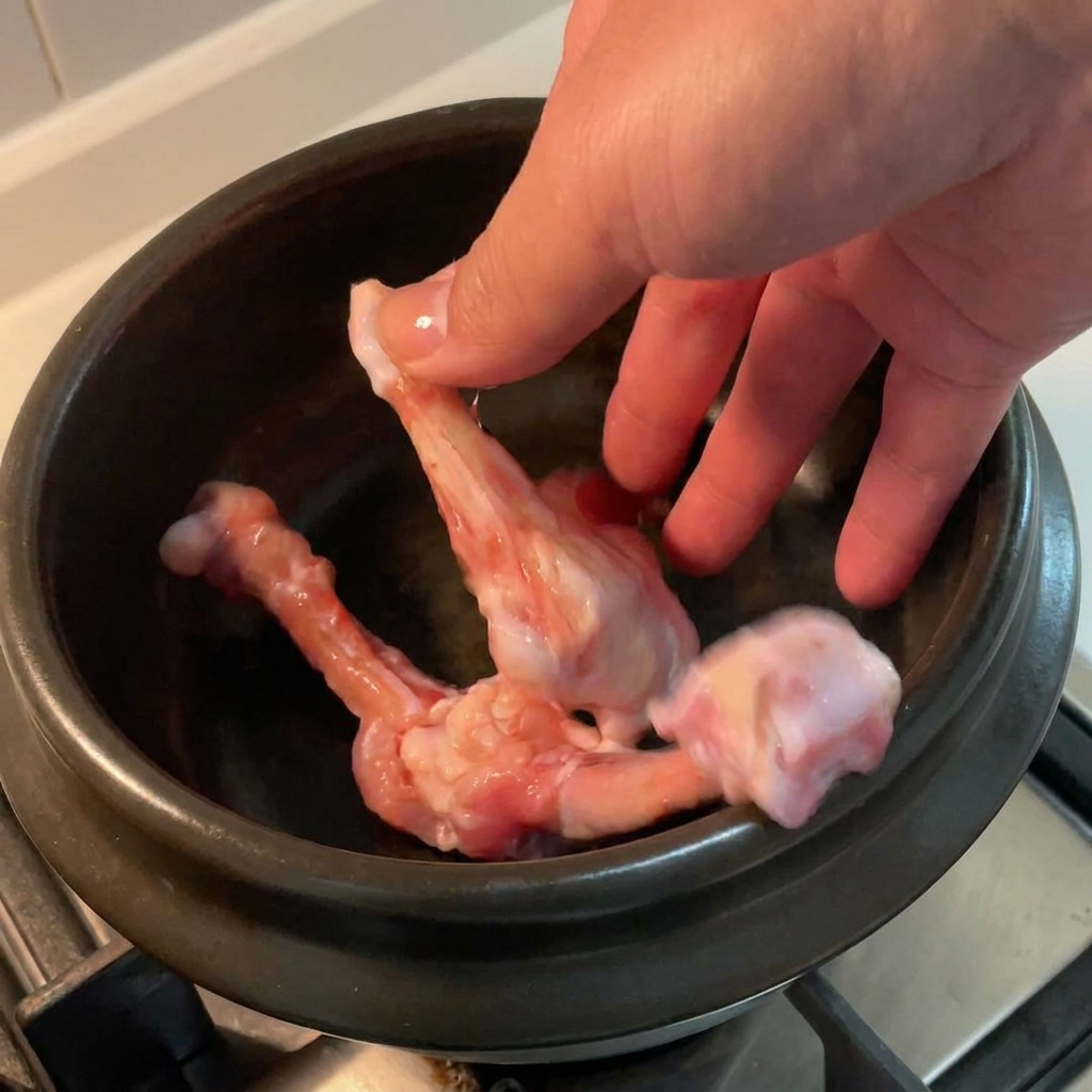 Raw chicken bones being arranged inside a black ceramic cooking pot.