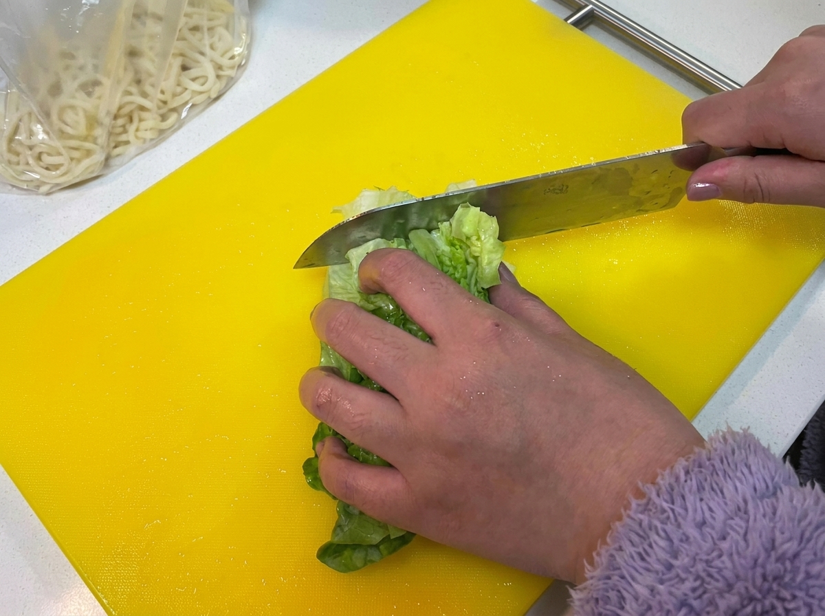Fresh green lettuce leaves being chopped on a bright yellow cutting board.