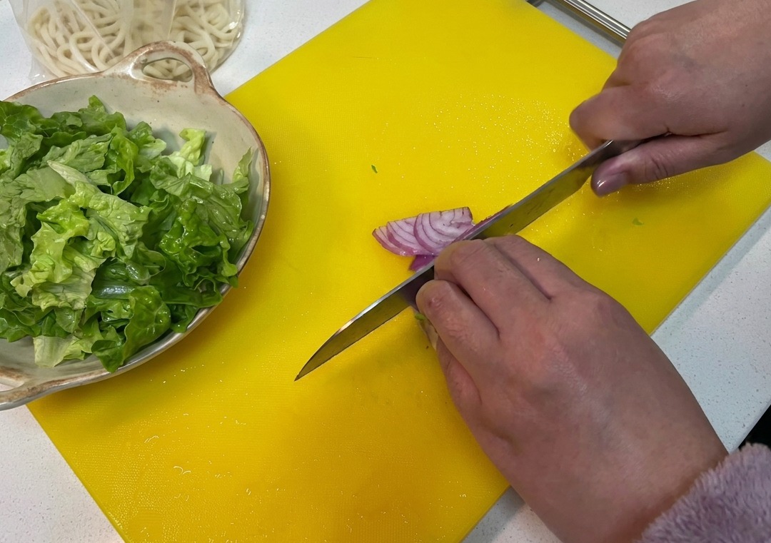 A red onion being sliced into thin pieces on a bright yellow cutting board.