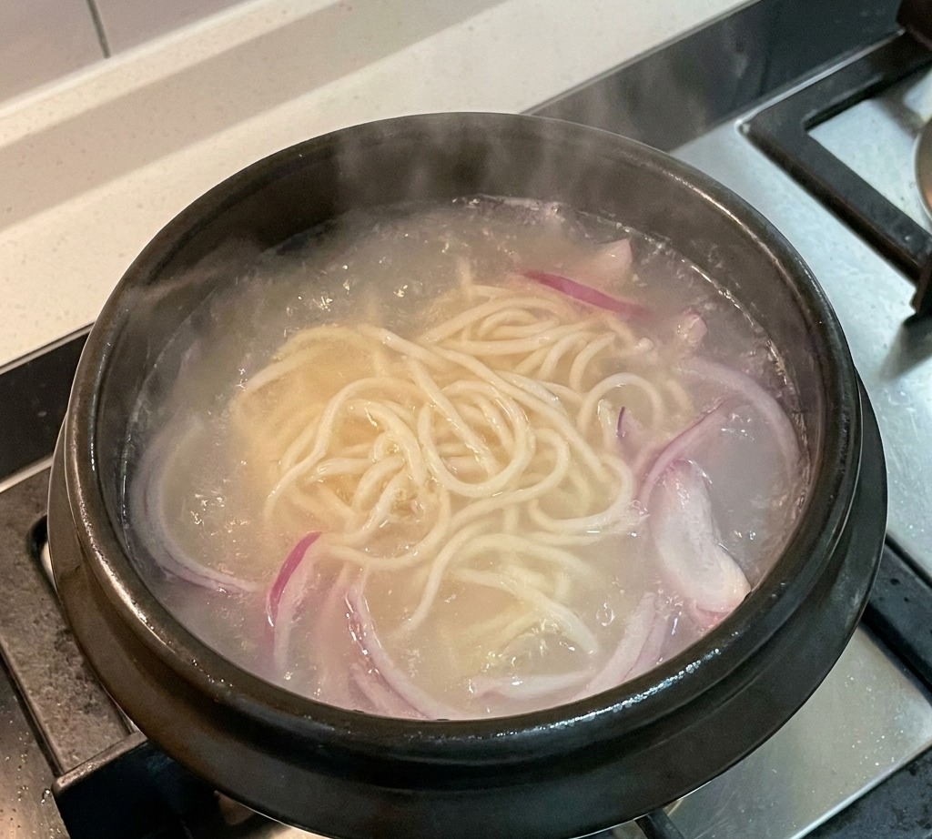 Sliced red onions simmering in a pot of broth with noodles.