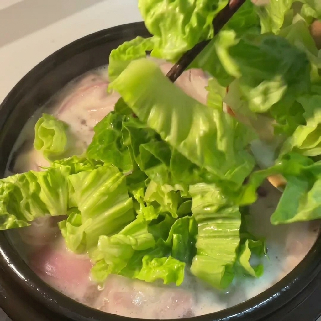 Fresh green lettuce being dropped into the simmering chicken soup with red onions.