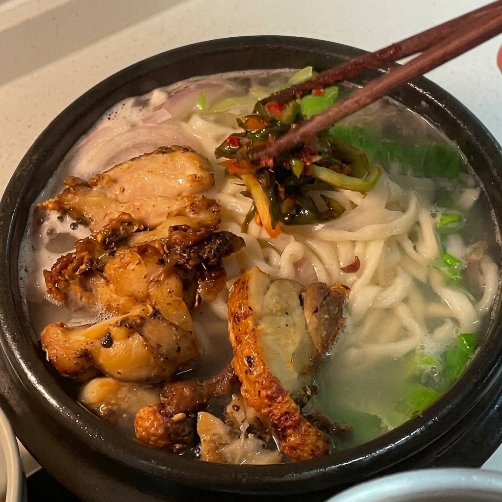 Vibrant red scallion kimchi being added as a garnish on top of the chicken noodle soup.