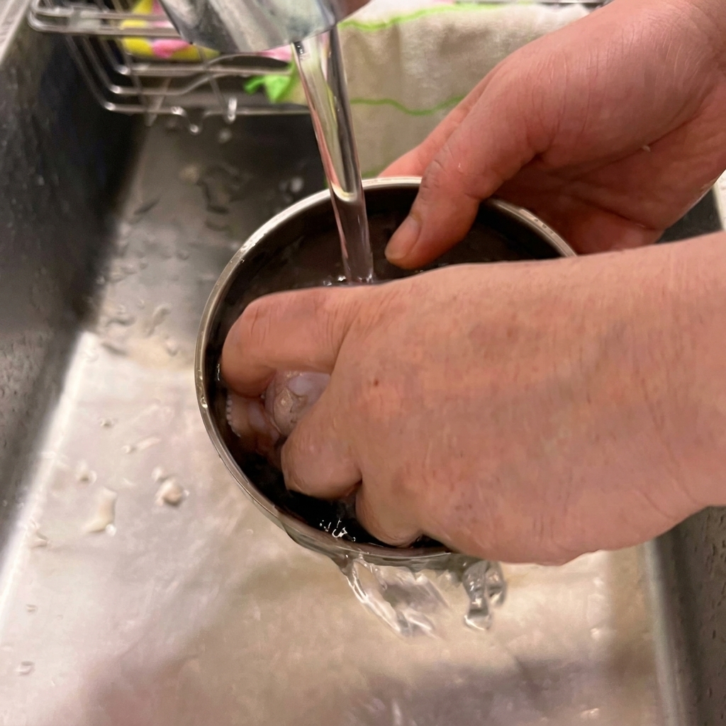 Fresh chicken wings being washed in a stainless steel bowl under a kitchen faucet.