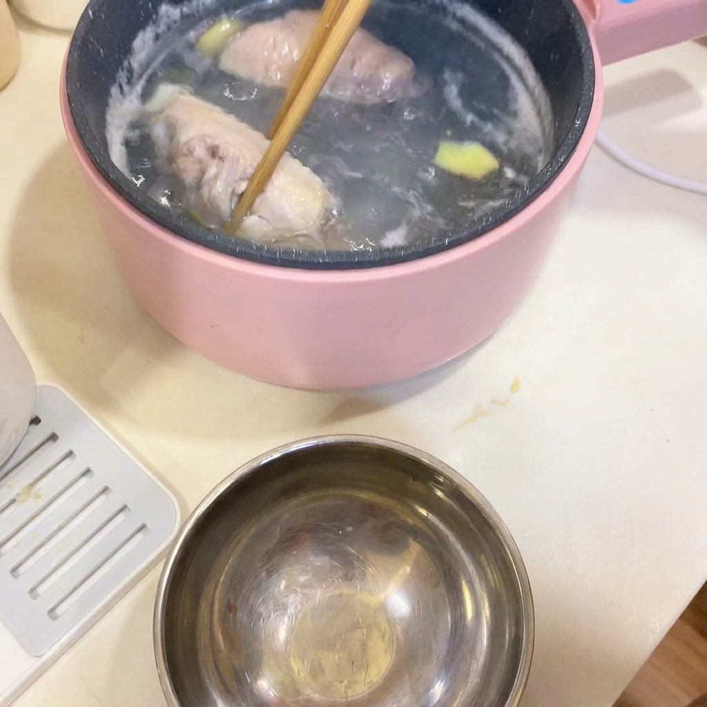 Chopsticks lifting blanched chicken wings out of the cooking pot.