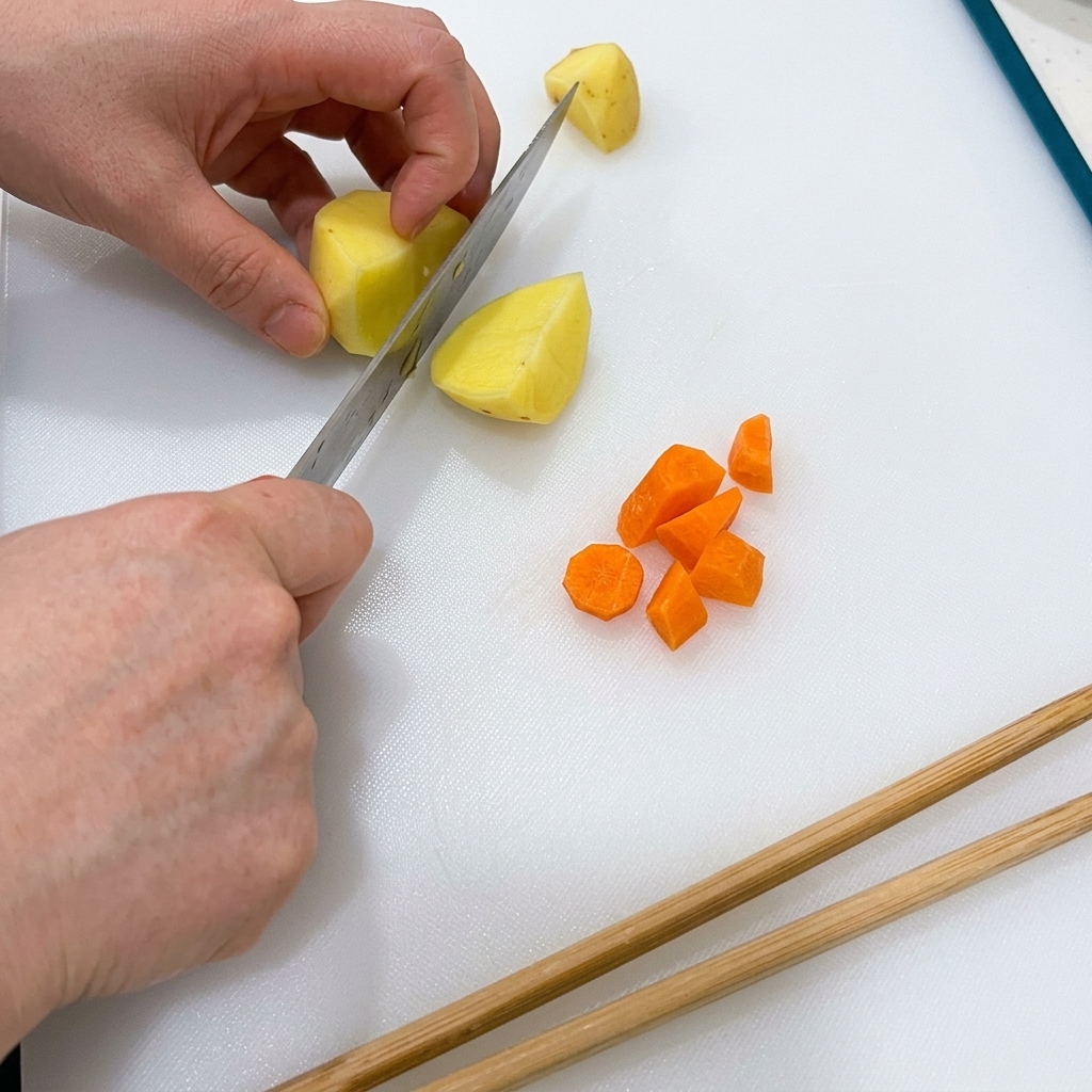 Carrots and potatoes being neatly diced on a clean white cutting board.
