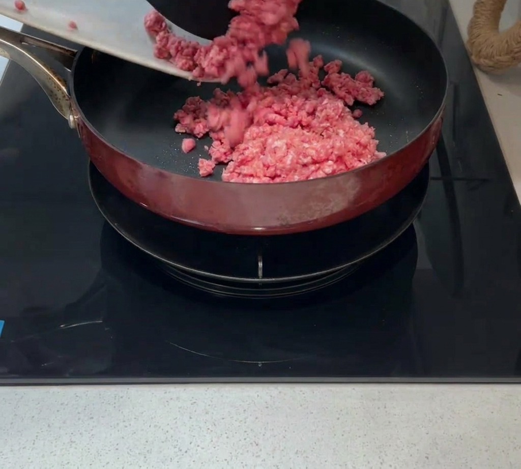 Raw minced meat being added to a hot pan with a small amount of oil.