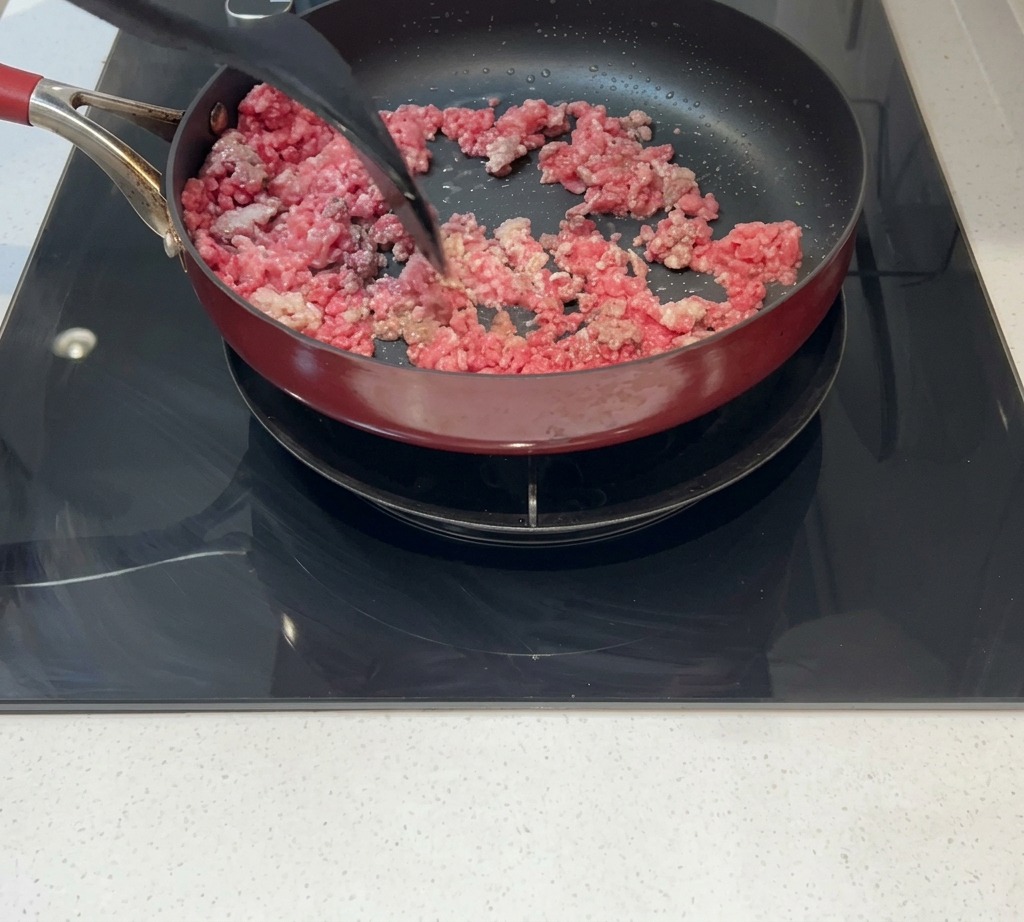 Minced meat being stirred in a pan until browned and fully cooked.