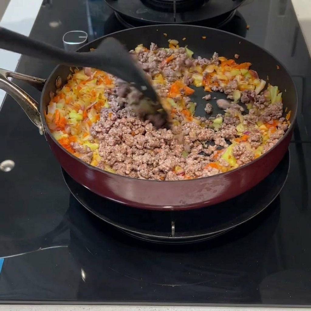 Minced meat and diced vegetables being stirred together in a pan with a black spatula.