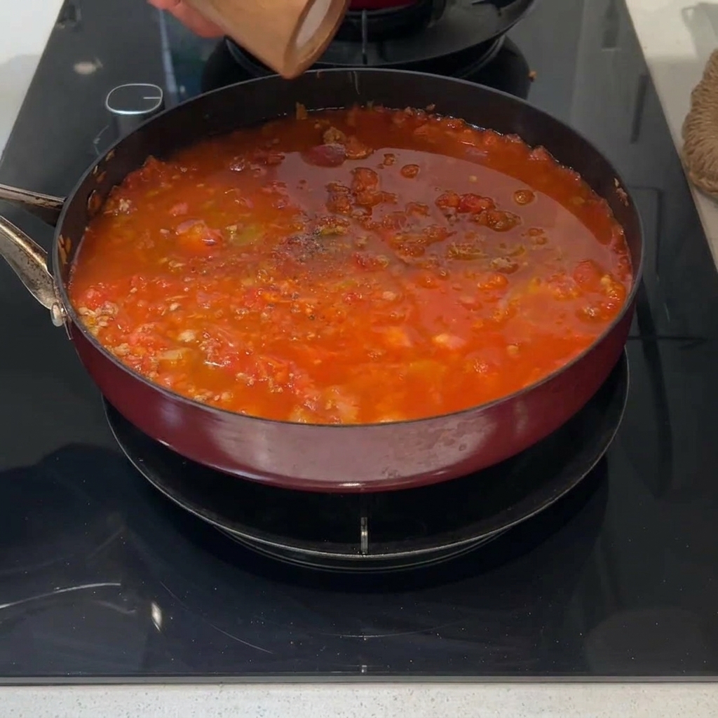 A fresh green sprig of rosemary placed on the surface of a simmering red meat sauce.
