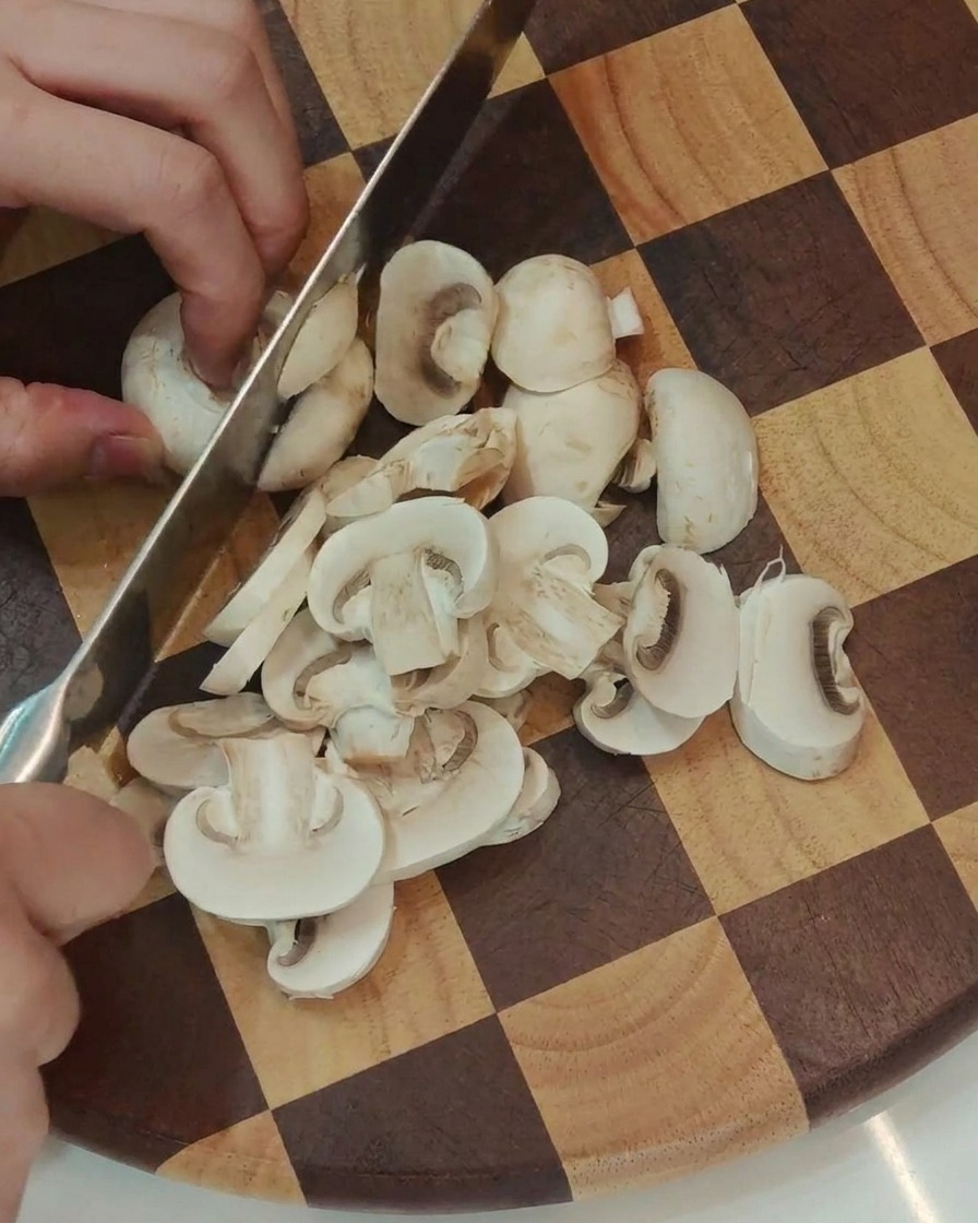 Fresh white button mushrooms being sliced into uniform pieces.