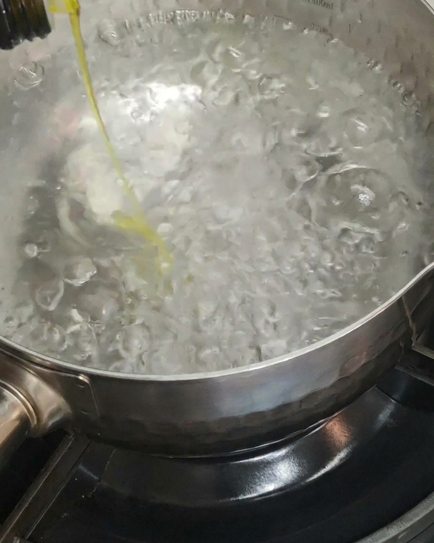 Olive oil being drizzled into a large pot of boiling water.