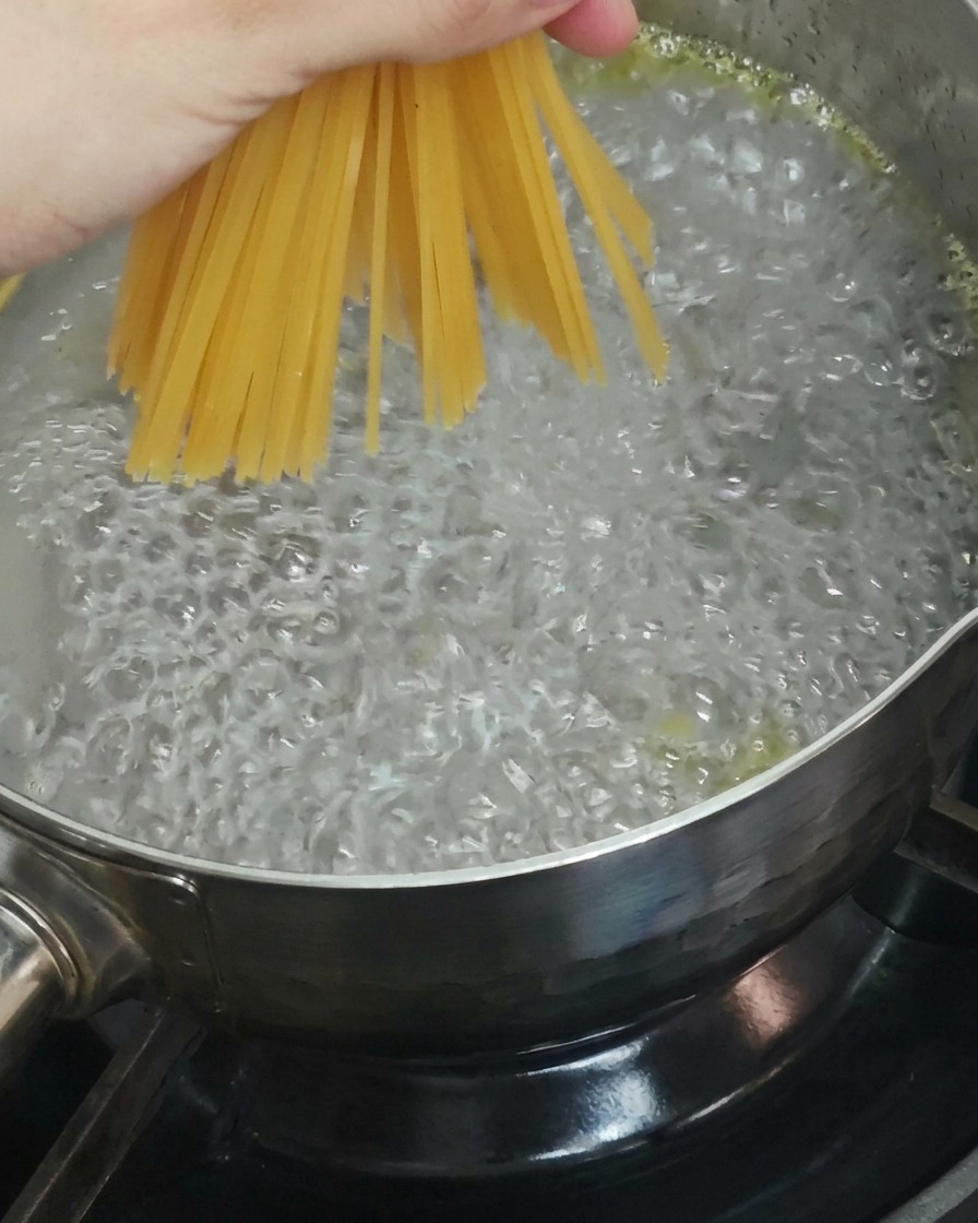 A close-up shot of a hand holding a bunch of dry spaghetti noodles and lowering them into a pot of bubbling boiling water.