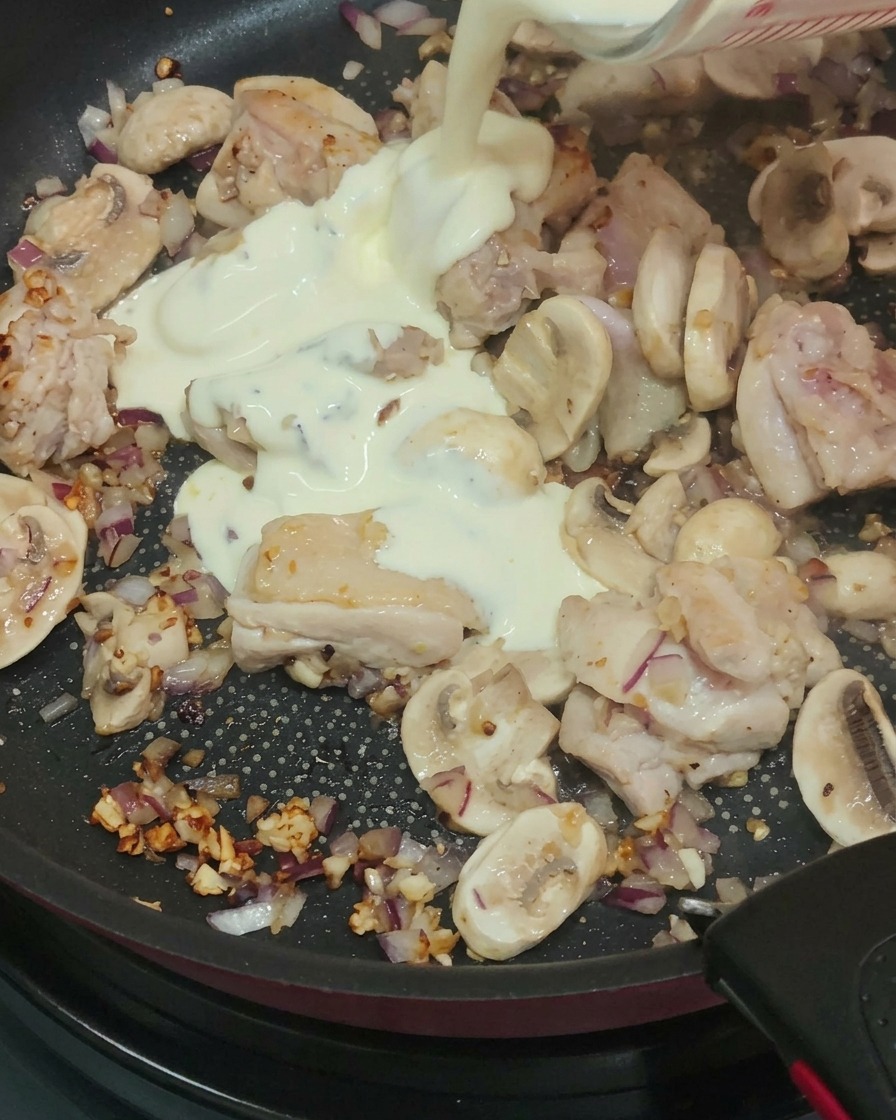 Cream, milk, and white wine being poured into the pan containing cooked chicken and sautéed mushrooms and onions.