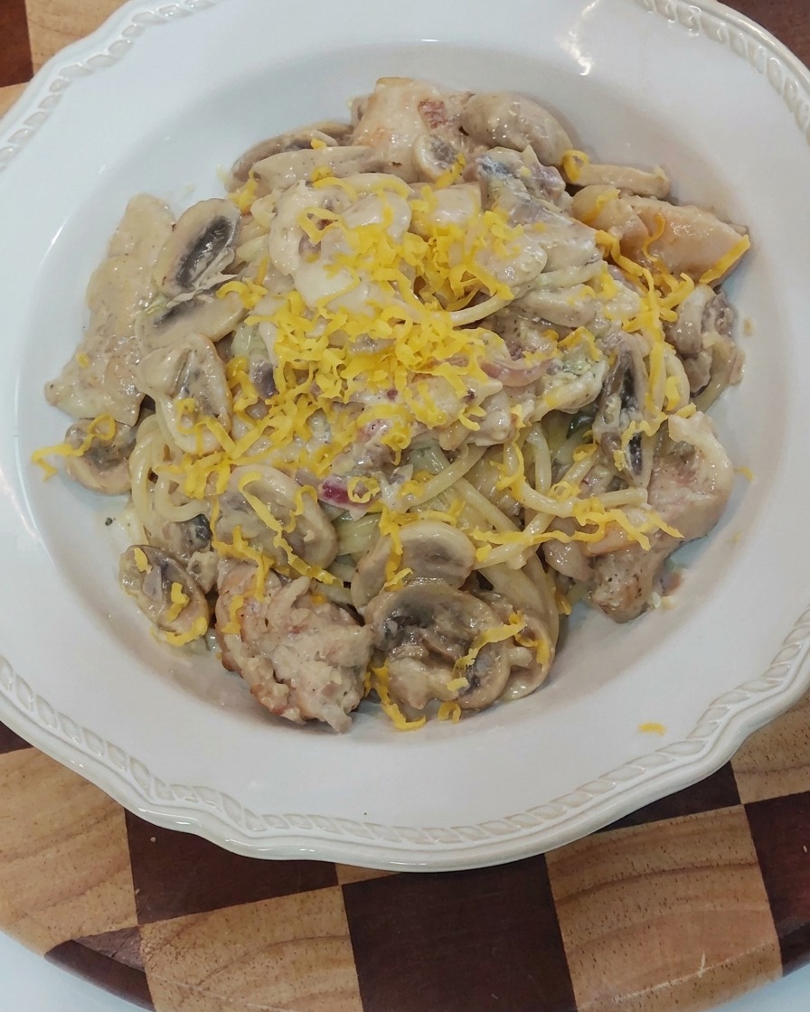 A block of yellow cheese being grated onto the plated creamy pasta.