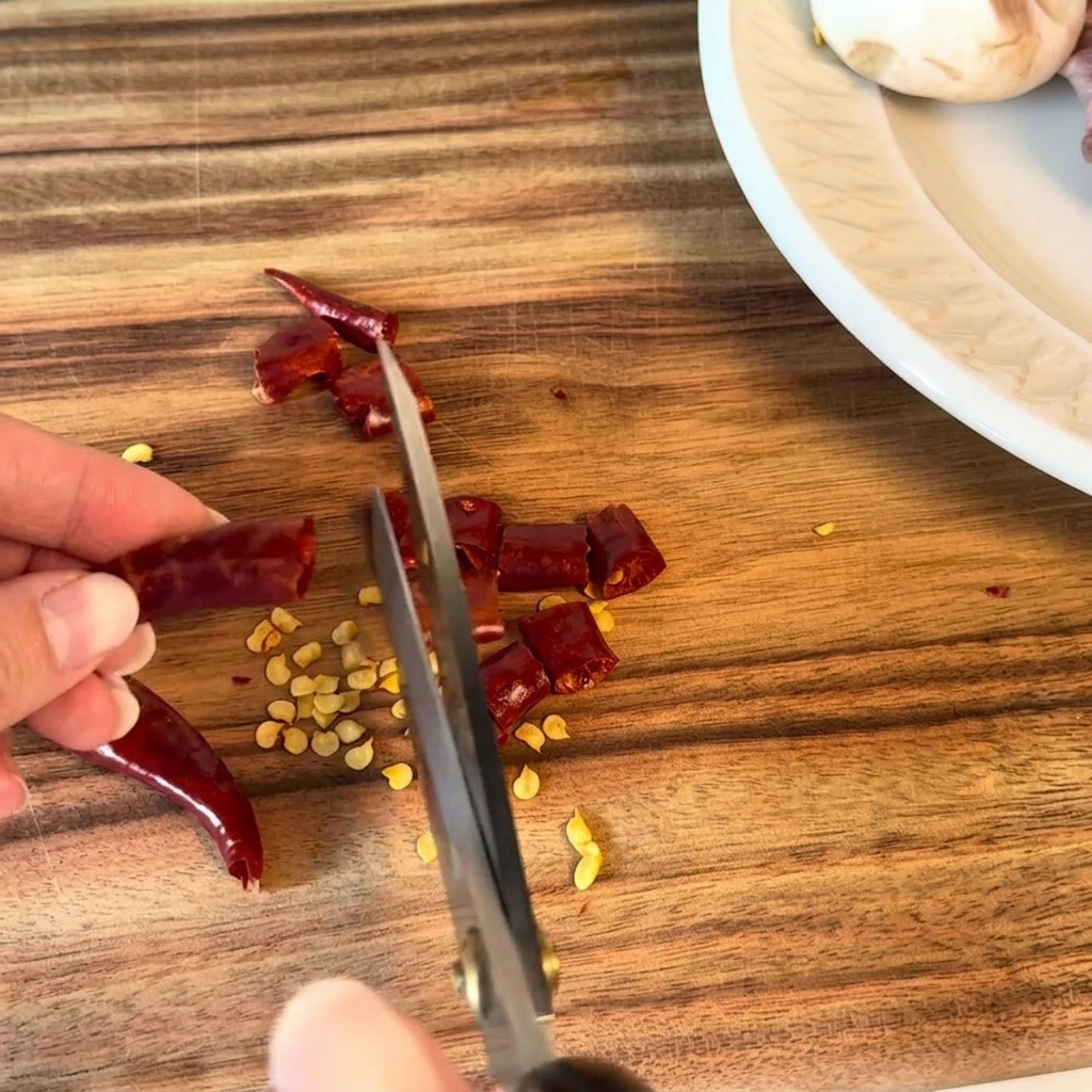 Dried chili peppers being cut into small pieces with kitchen scissors.