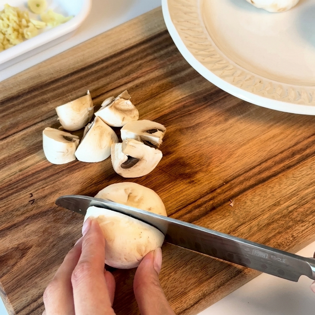 Fresh mushrooms being chopped into halves and quarters on a wooden board.