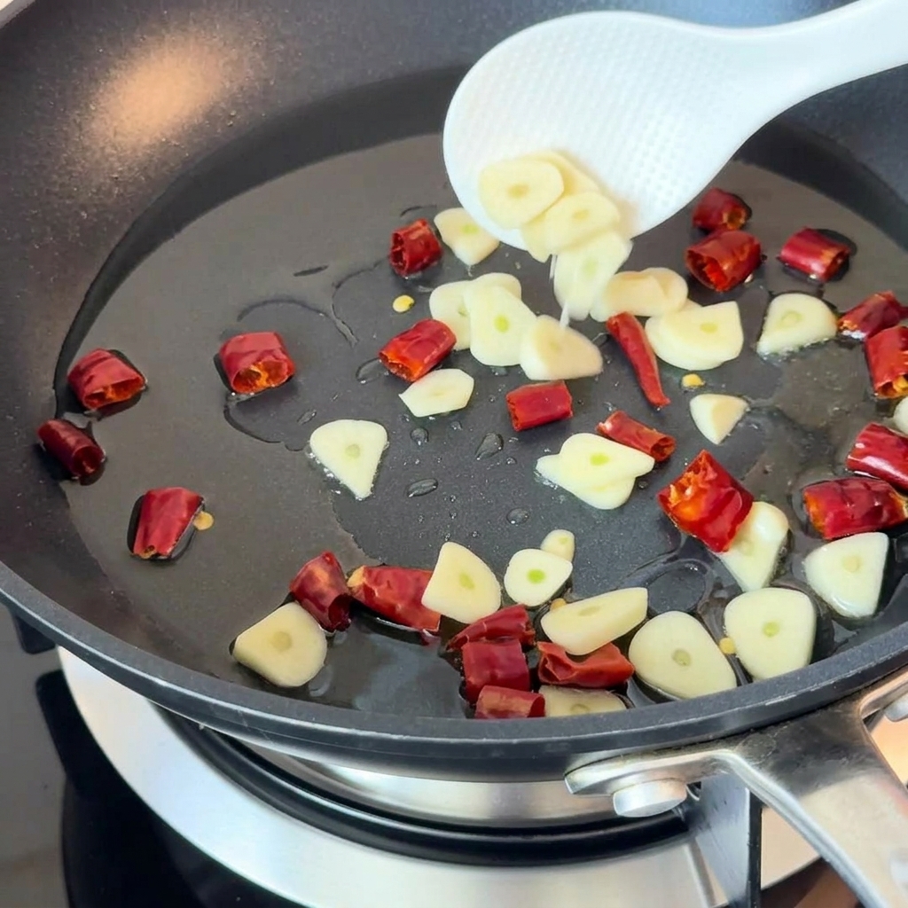 Sliced garlic and dried chili peppers sautéing in hot oil in a pan.