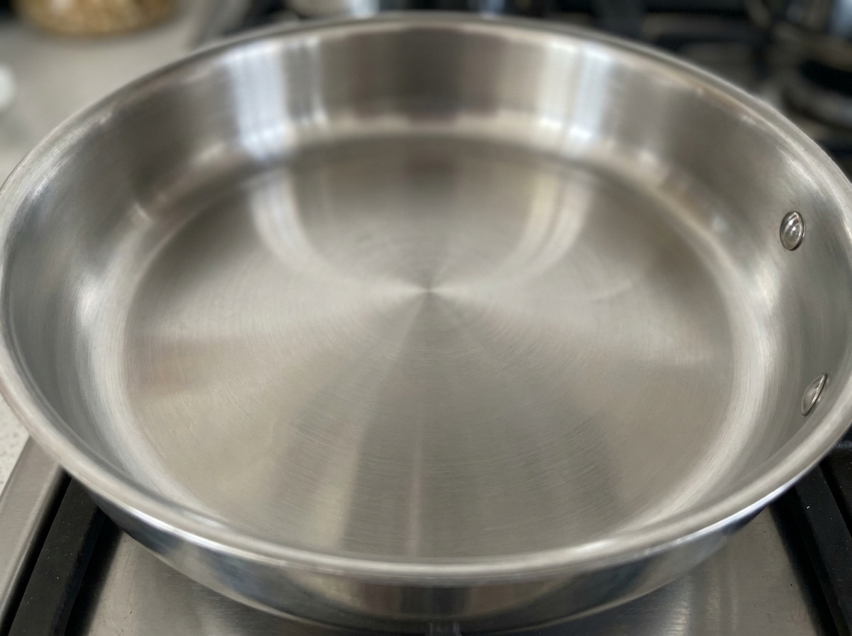Black peppercorns heating in a dry pan on a stovetop.