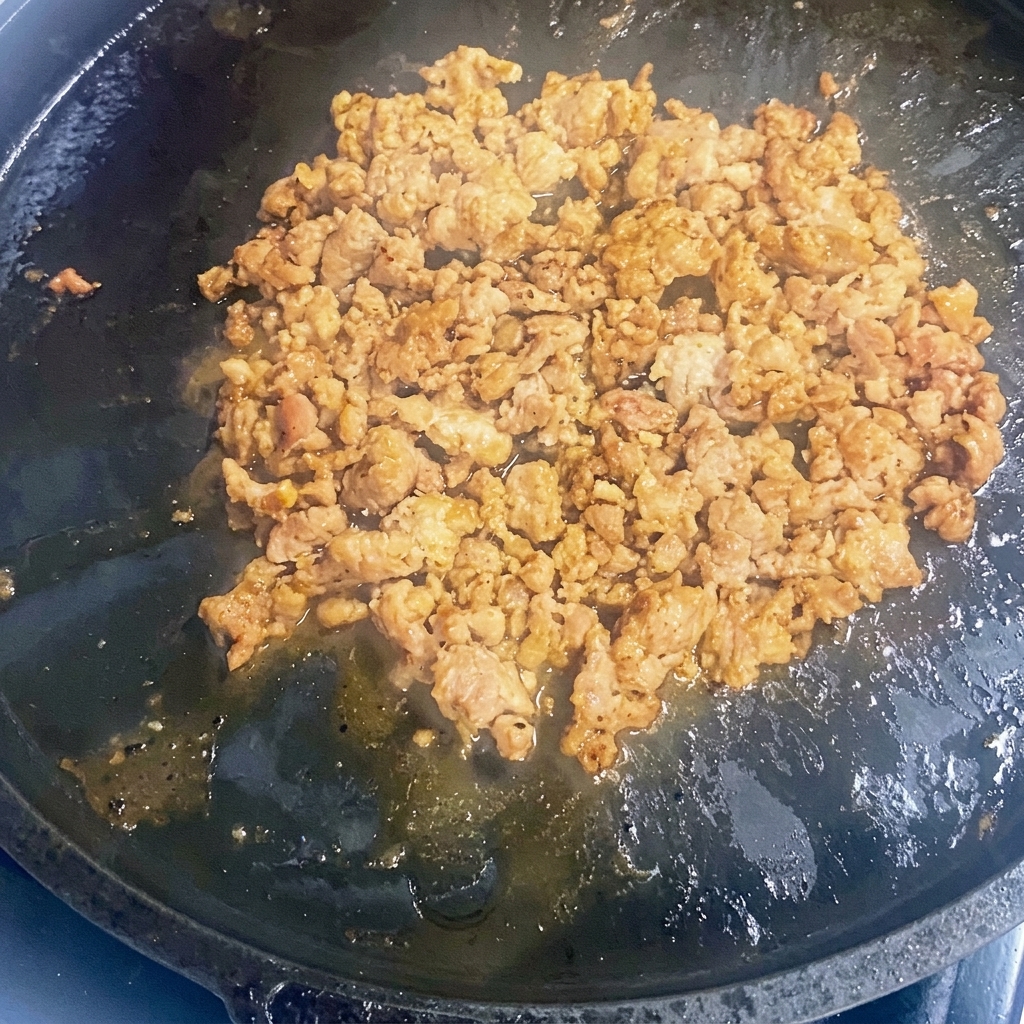 Ground meat browning in a hot cast-iron skillet.