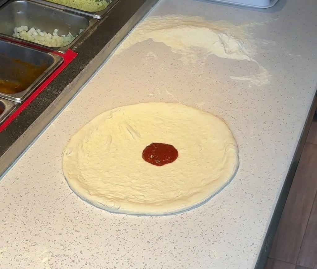 A dollop of rich red tomato sauce placed in the center of a stretched pizza crust on a countertop.