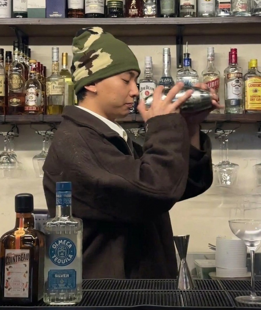 A bartender vigorously shaking a cocktail shaker to chill the ingredients.