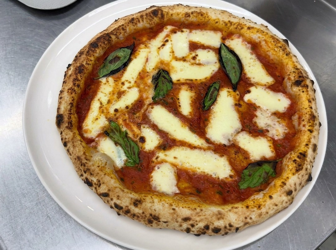Hands carefully stretching a ball of proofed pizza dough on a floured countertop into a perfect round crust.