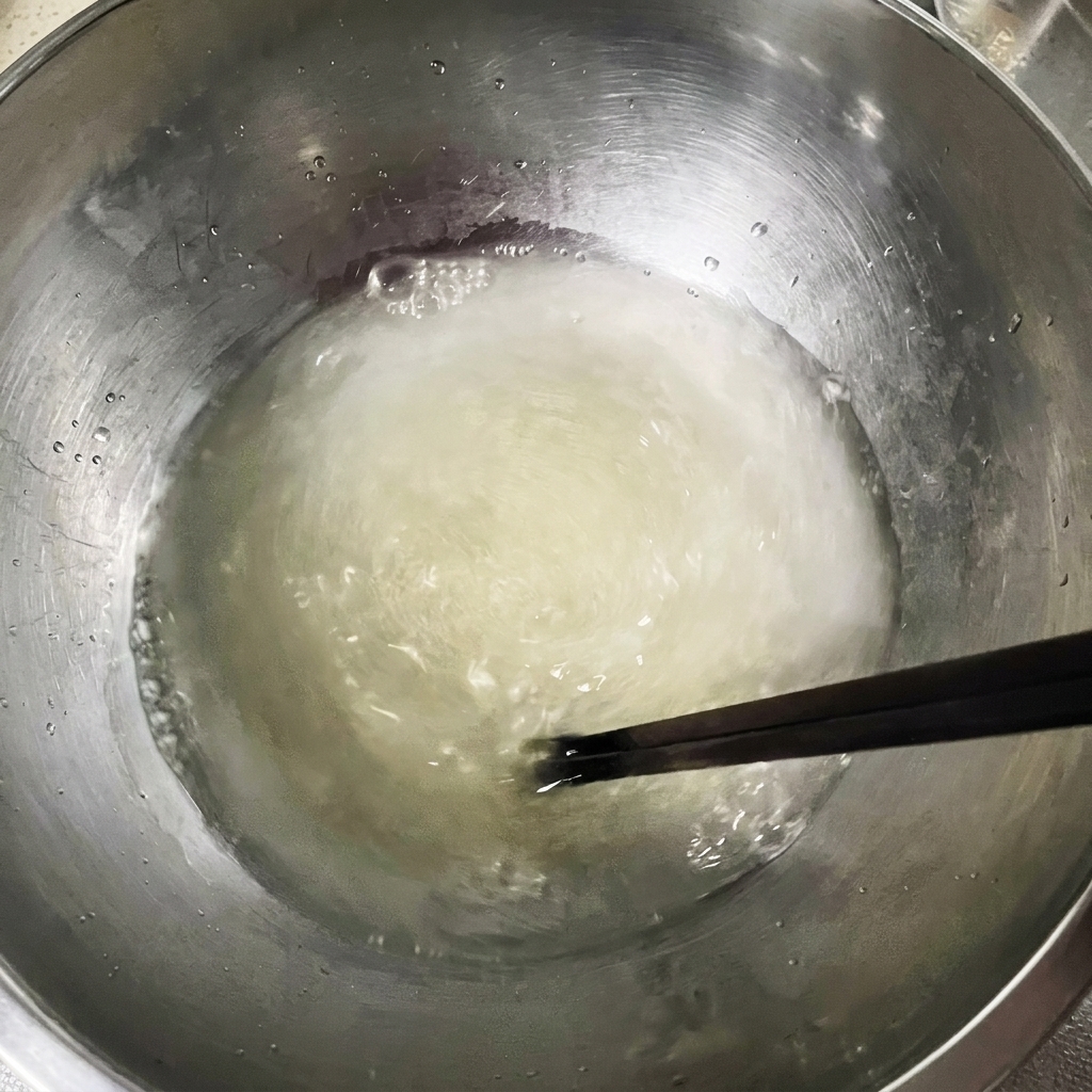 Chopsticks stirring a slightly cloudy mixture of water, yeast, and salt in a large metal bowl.
