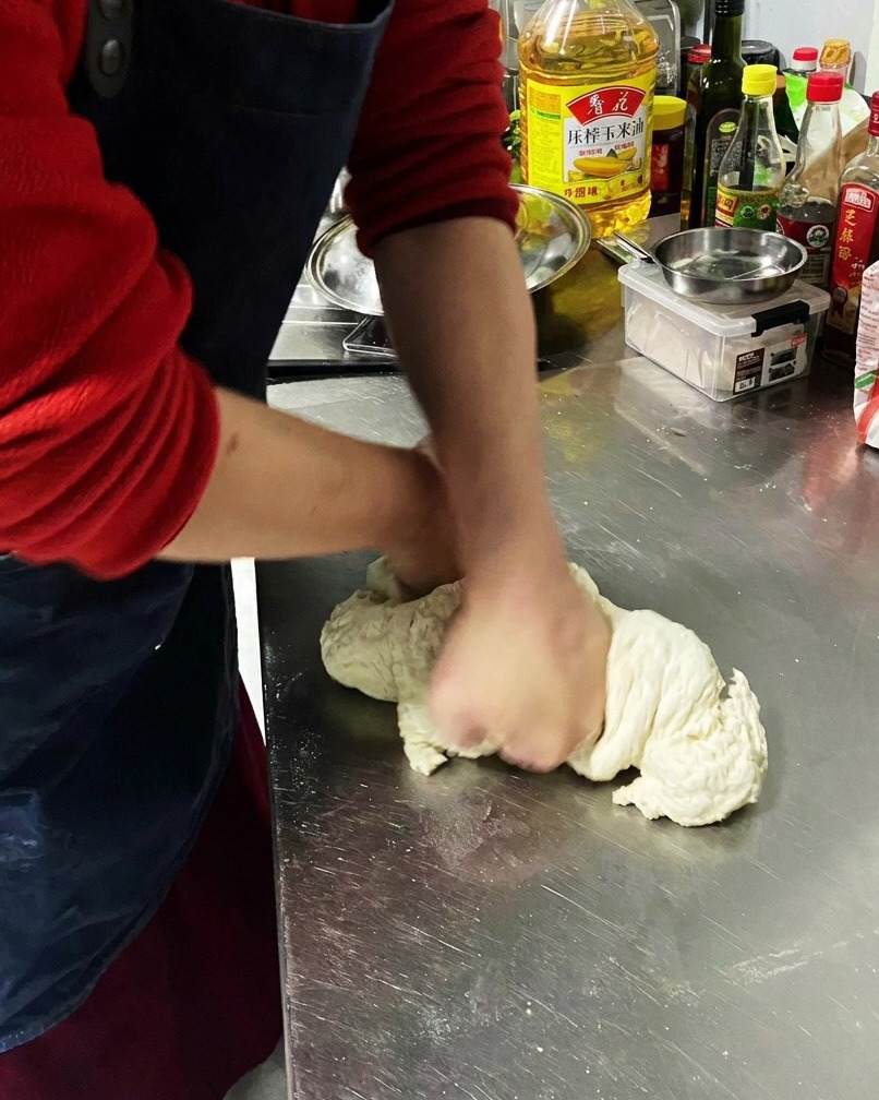 Close-up of dough being kneaded on a stainless steel surface, showing a smooth, elastic texture.