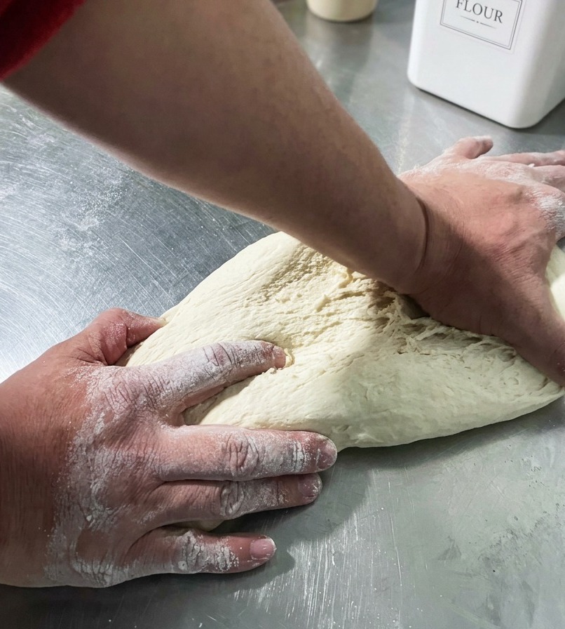 Hands shaping a smooth, round ball of pizza dough on a work surface.