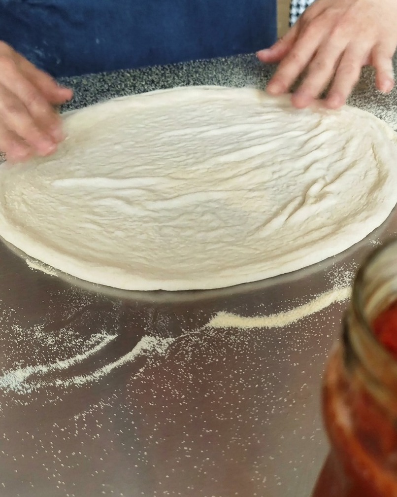 Circular pizza dough pressed flat on a semolina-dusted work surface.