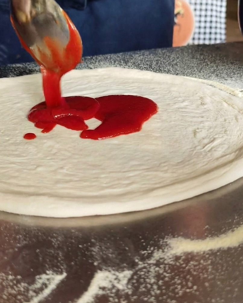Tomato sauce being spread in a circular motion over the center of the pizza dough.