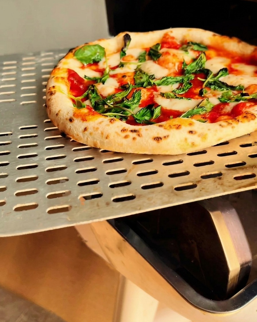 A freshly baked Margherita pizza with a perfect, airy, charred crust being lifted from the oven on a metal peel.