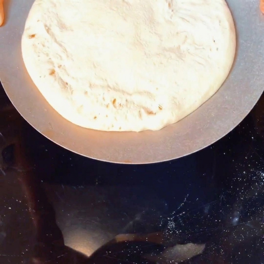 A ball of raw pizza dough being coated with yellow cornmeal in a container.