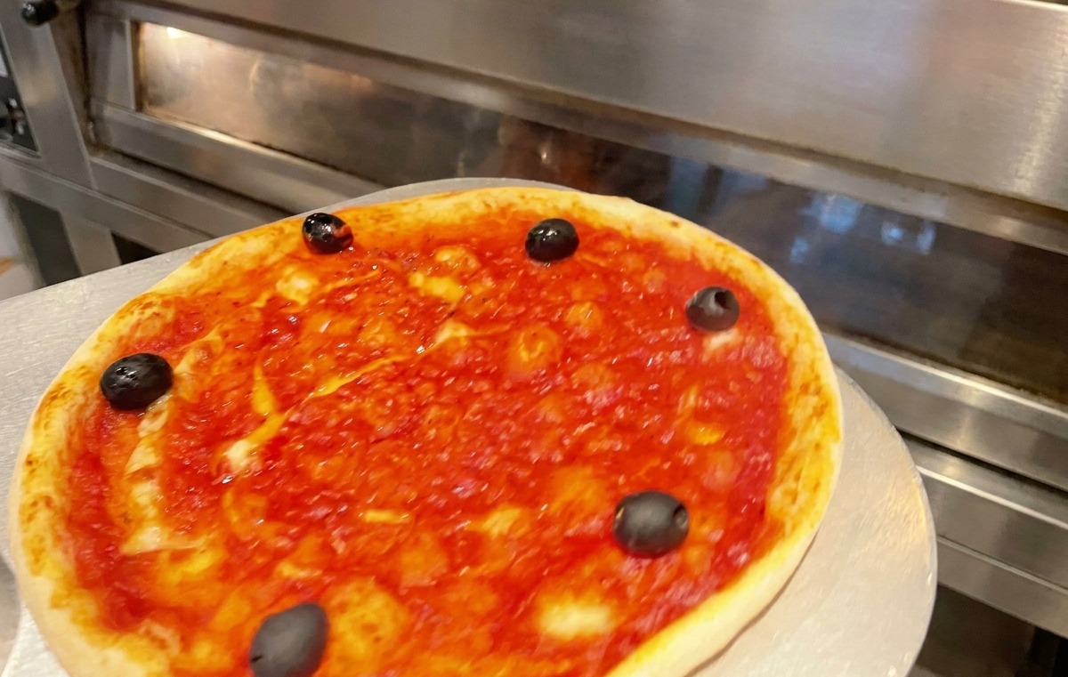 A pizza pan being slid into a hot commercial oven for baking.