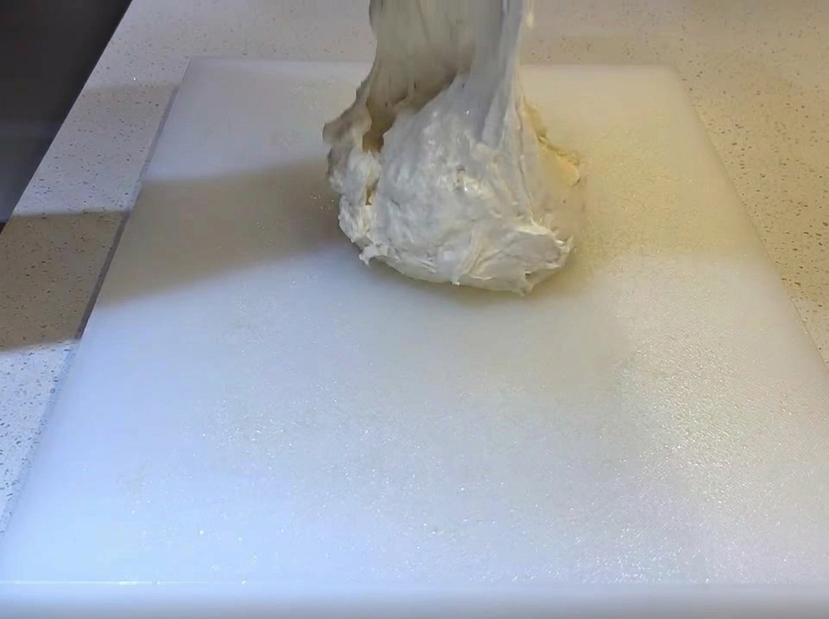 Soft, sticky dough being dropped onto an oiled white cutting board.