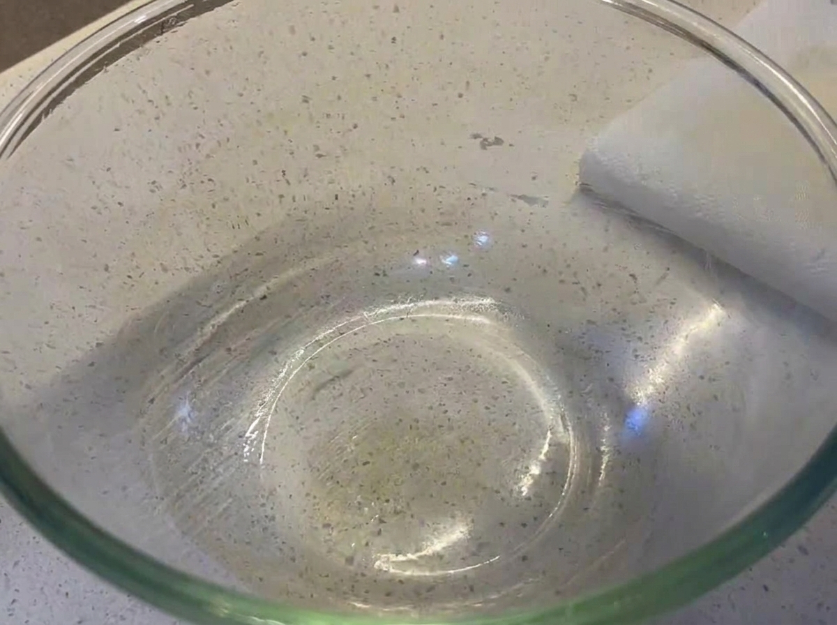 A smooth, round ball of pizza dough resting inside a clear glass mixing bowl lightly coated with oil.