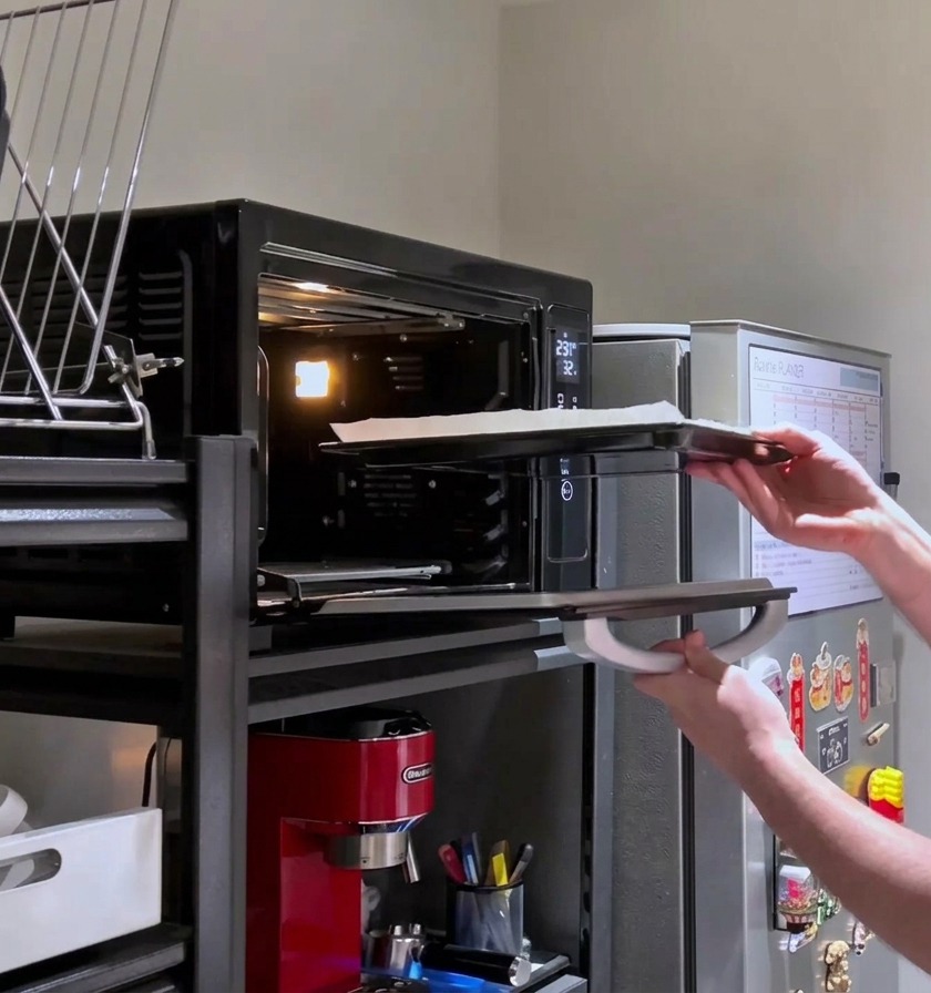 A person placing a cheese-loaded rectangular pizza back into the hot oven for its final bake.