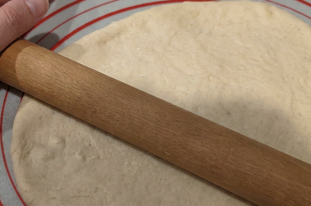 Dough being rolled into a flat circle on a non-stick silicone mat.