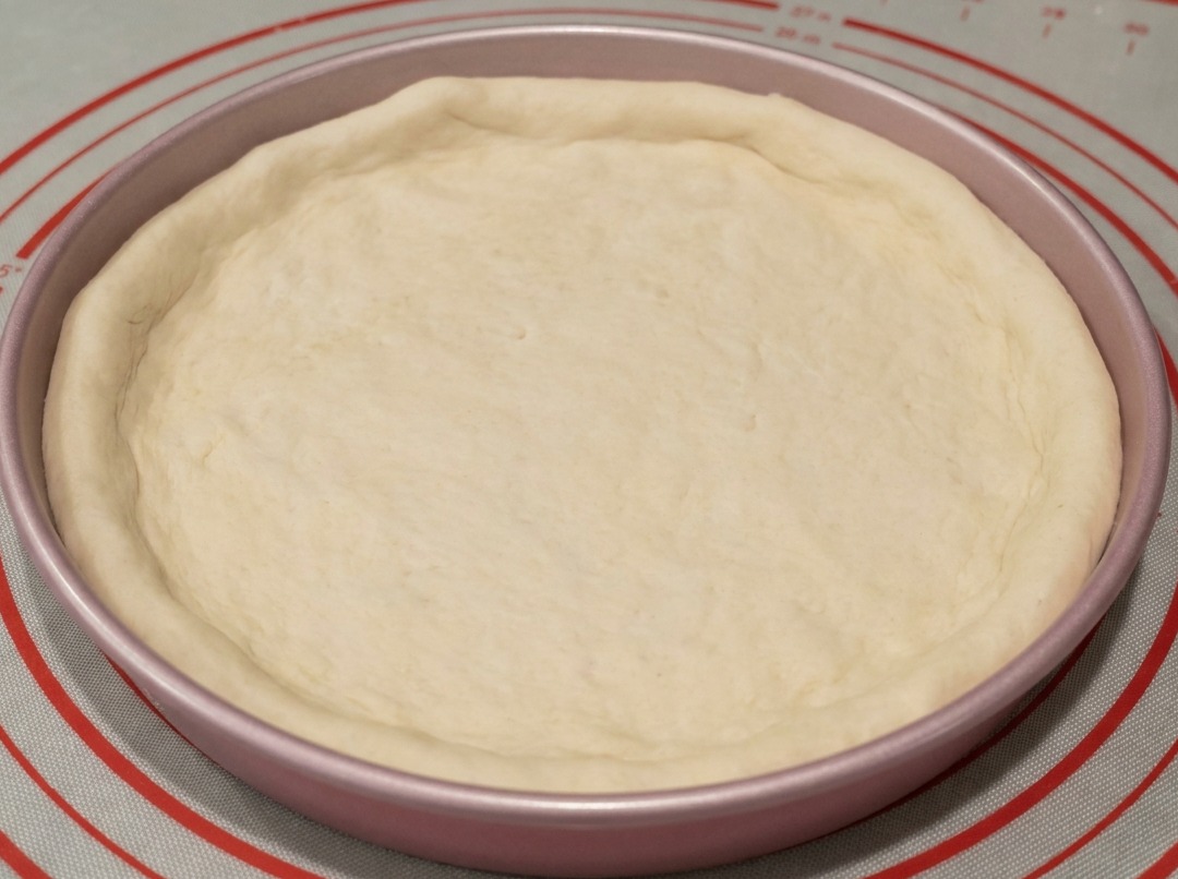 Dough fitted into a 9-inch metal pizza pan with edges shaped by hand.