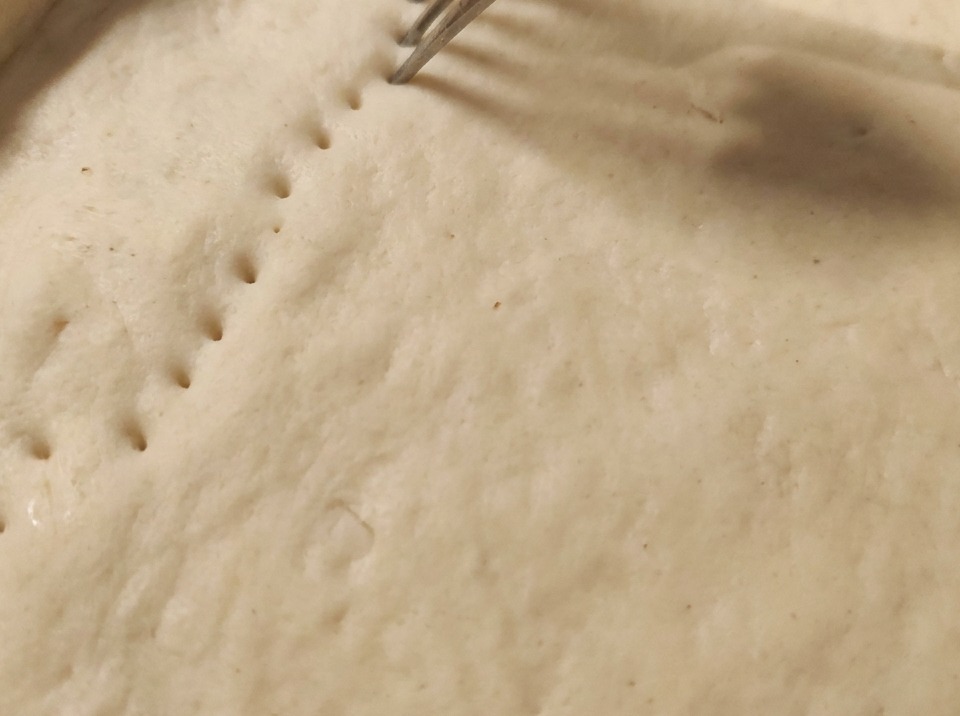 A fork pressing into raw dough to create rows of holes across the crust.
