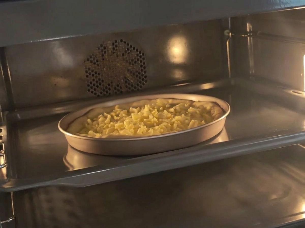 A pan containing prepared pizza dough topped with shredded cheese sitting inside a preheated oven.