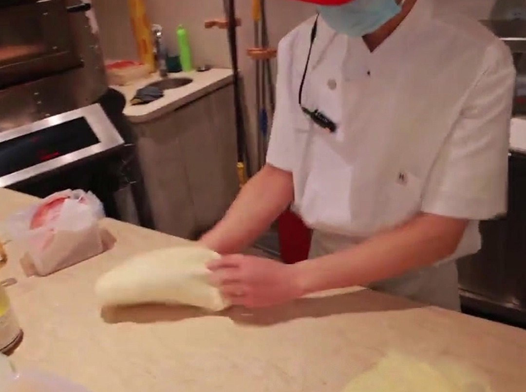 A chefs hands stretching a ball of pizza dough on a floured marble countertop.
