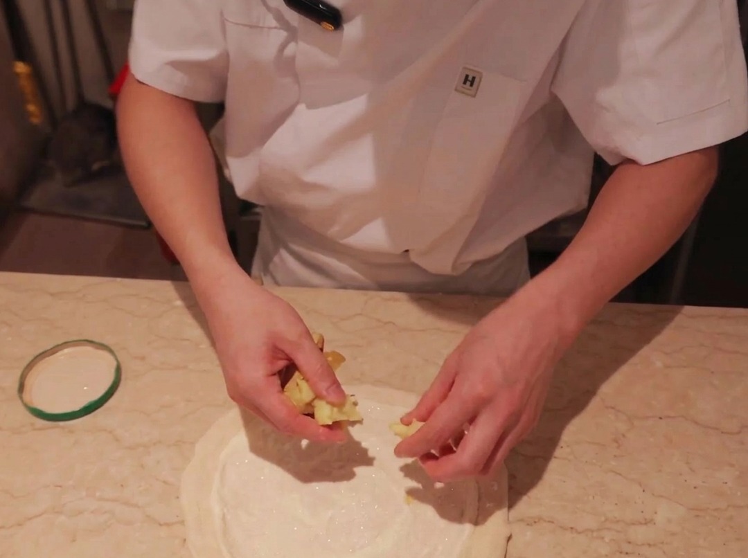 Thinly sliced potatoes being placed on top of a sauce-covered pizza dough base.